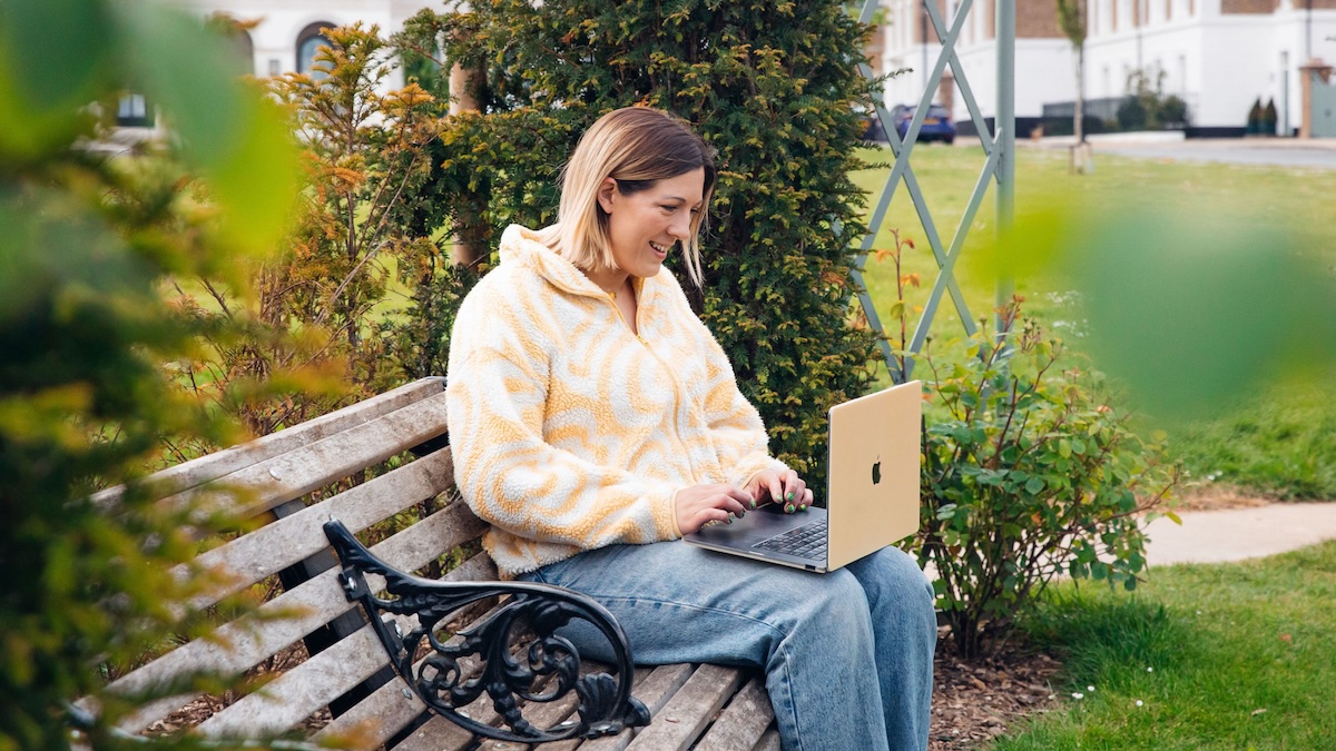 Beth Carter gestures to her laptop screen while sitting on a park bench