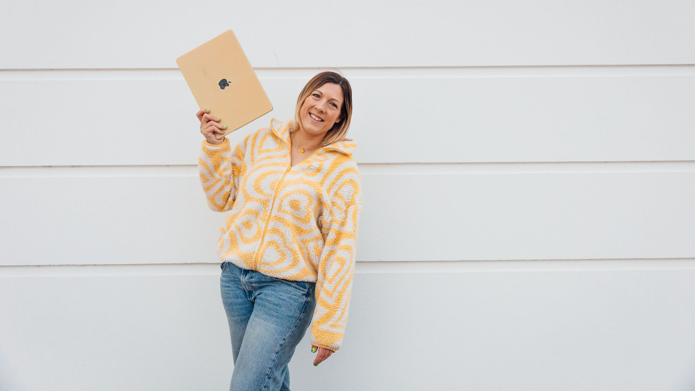 Beth Carter waves her laptop in the air with her right hand against a white background